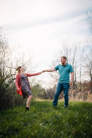 A couple holding hands and dancing in a grassy field on a bright spring day.