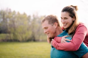 A couple shares a piggyback ride moment in a spring field.