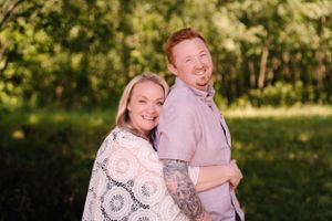 A playful couple poses while hugging and laughing in a sunny outdoor setting.