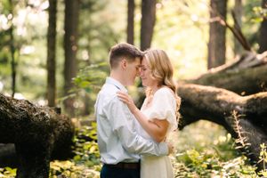 A romantic moment captured between a couple in white attire against a sunlit forest backdrop.
