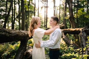 A couple in formal attire shares an intimate dance in a wooded setting with natural light.