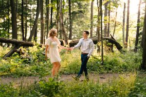 A couple enjoys a playful dance together on a woodland trail surrounded by summer foliage.
