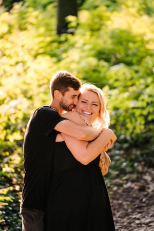 Two people share a joyful moment hugging and laughing in a forest setting with dappled sunlight.