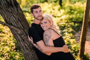 A romantic portrait of two people leaning against a tree trunk in golden afternoon light.