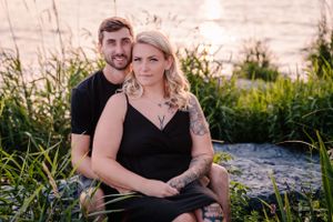 A romantic couple's portrait captured at sunset among waterfront grasses and rocks.