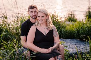 Two people share an intimate moment on rocks by the water during golden hour.