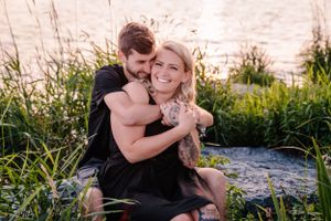Joyful couple sharing a tender moment on rocks by the water during golden hour.