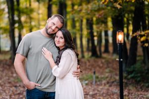 A couple embraces while posing for a romantic portrait in a fall forest setting.