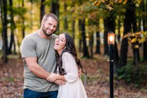 A playful couple shares a laugh together in an autumn forest with a lantern post in the background.