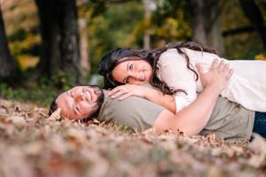 A couple lies in fallen autumn leaves sharing a playful moment together.
