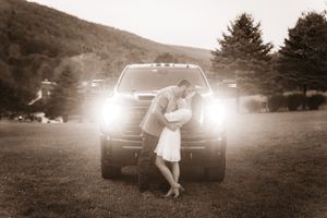 A black and white photo of a couple embracing in front of a truck with glowing headlights.