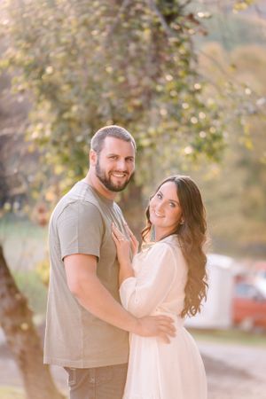 A romantic couple embraces on a sunlit path during an engagement photo session.