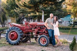 A couple stands beside a classic red Farmall tractor against a rural backdrop.