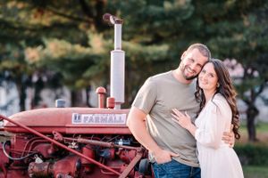 A couple poses together in front of a vintage red Farmall tractor during their engagement shoot.