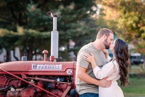 A couple shares an intimate moment while posing with an antique red Farmall tractor.