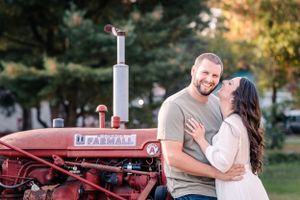 A couple shares a tender moment while posing by a vintage red Farmall tractor.