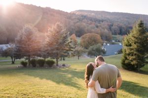 A couple walks together on a hillside during golden hour with mountains in the distance.