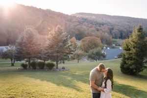 A romantic couple shares an intimate moment on a hillside during golden hour with autumn trees in the background.