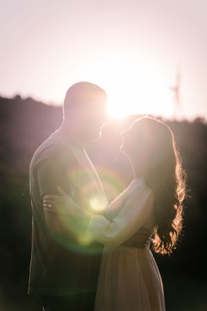 A couple embraces in silhouette against a bright sunset creating a romantic backlit effect.
