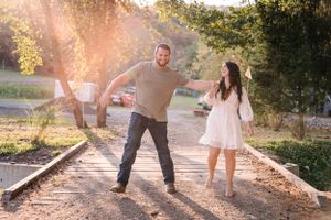 A playful couple laughs and dances on train tracks during a sunset photoshoot.