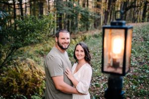 A romantic couple poses together by an illuminated lantern in a forest setting.