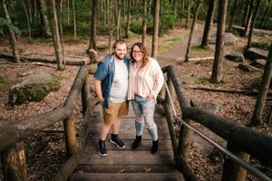Couple standing together on wooden bridge path through wooded forest area.