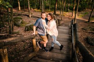 Playful couple posing on rustic wooden walkway in forest setting.