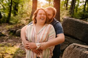 Couple embracing and laughing together in sunlit forest setting.