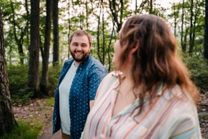 A couple shares joyful expressions while standing in a sunlit forest.