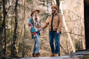 A couple in casual winter clothing having an intimate moment while standing on rocks in a forest setting.