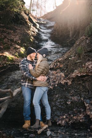 A couple sharing an intimate moment by a winter creek surrounded by rocks and bare trees.