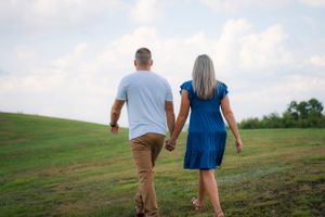 A couple walking hand in hand through a sunny hillside meadow.