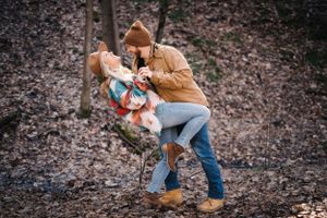 A couple sharing a playful moment in autumn woods while wearing cozy outerwear.