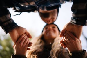 A creative low-angle shot of people holding hands in a circle formation viewed from below.