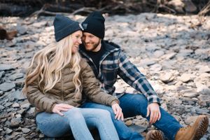 A couple in casual winter wear sharing an intimate moment while sitting on rocky ground.