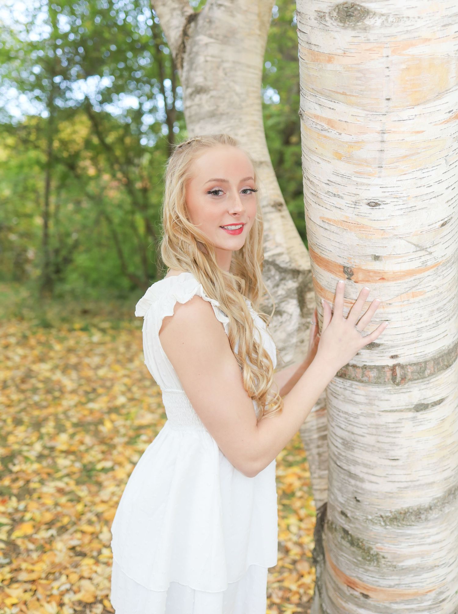 Portrait by a white birch tree with autumn leaves scattered on the ground.