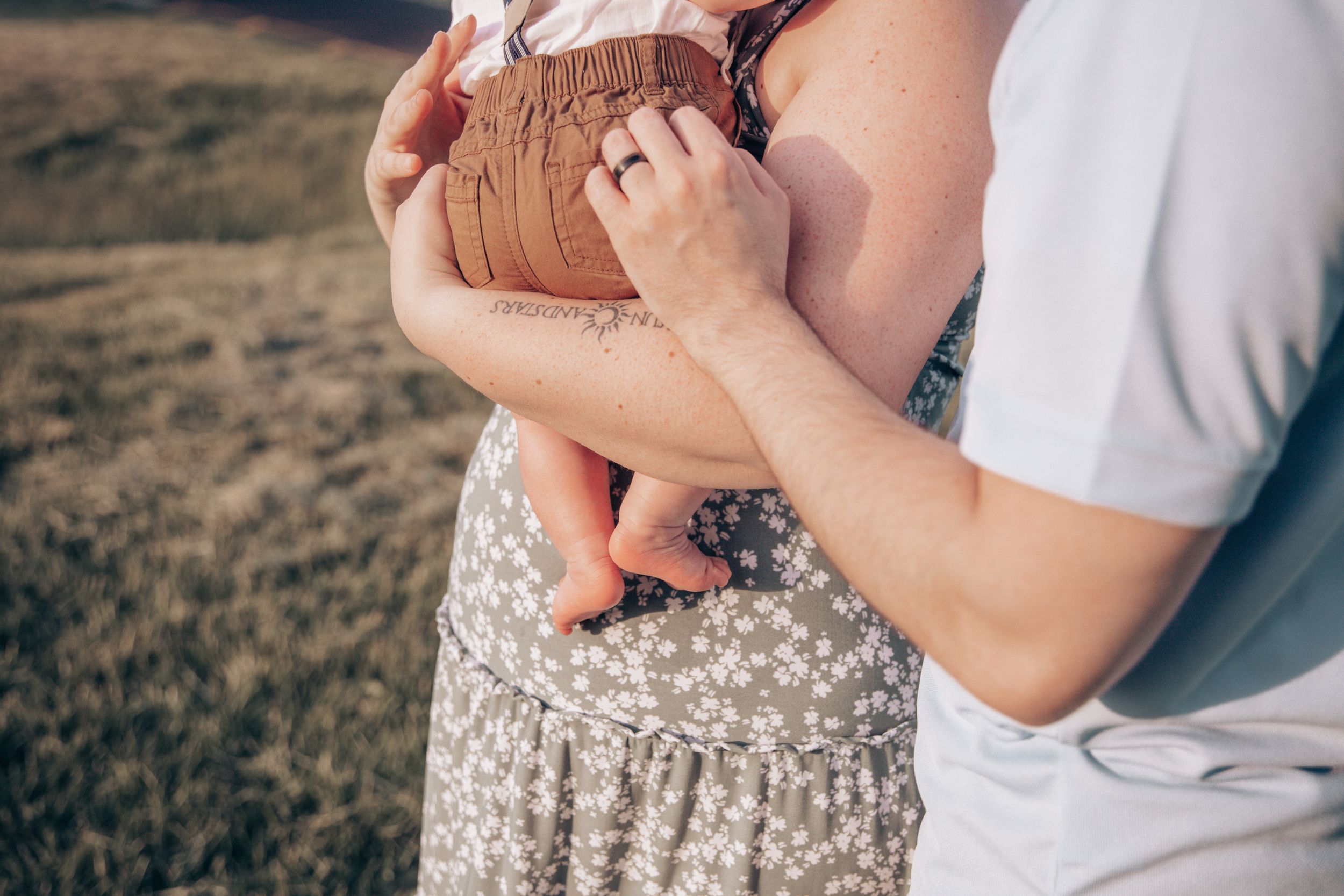 Close-up of hands holding a baby against a floral dress in a field.