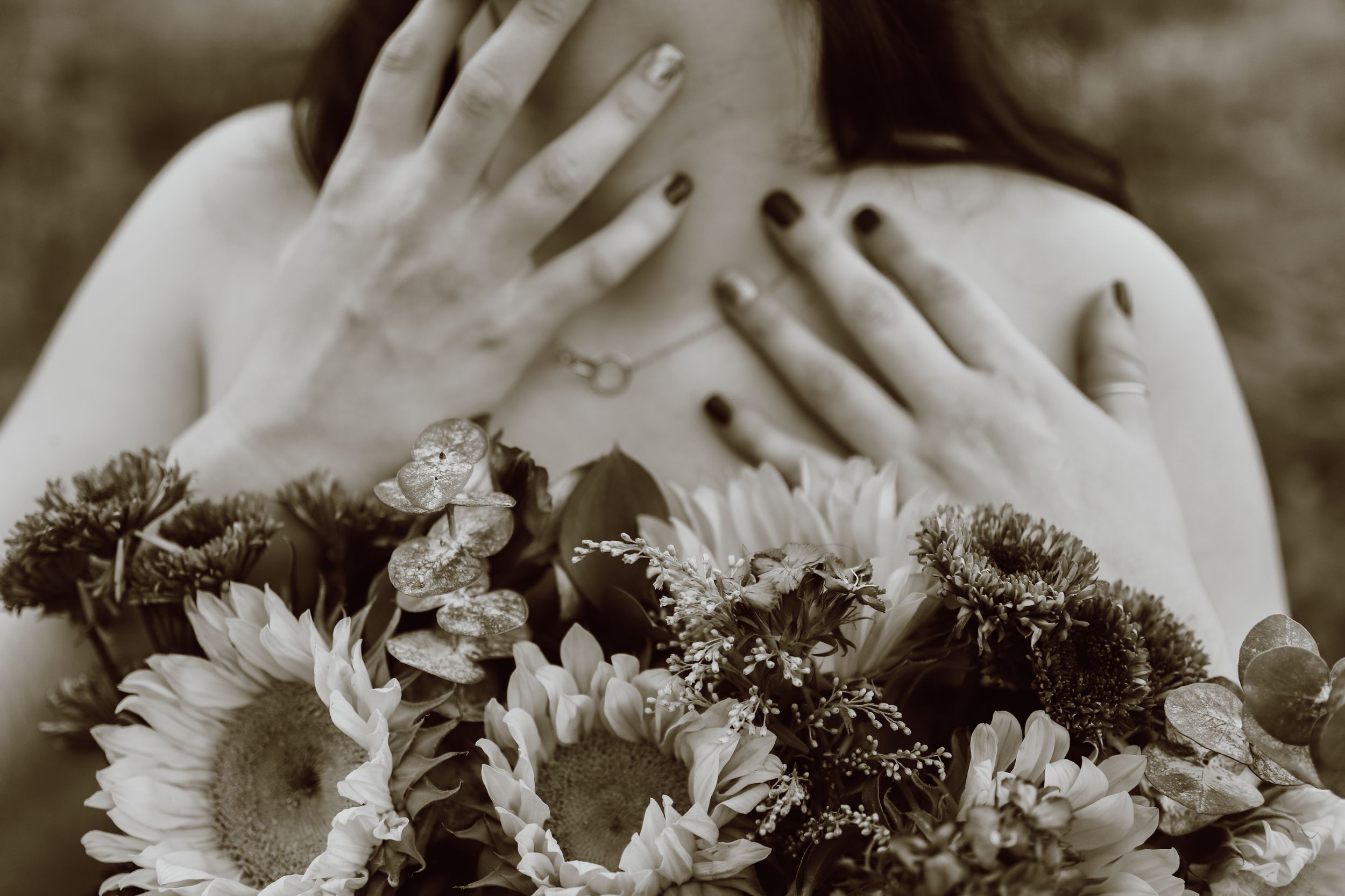 Artistic black and white photo of hands reaching up with sunflowers in the foreground.