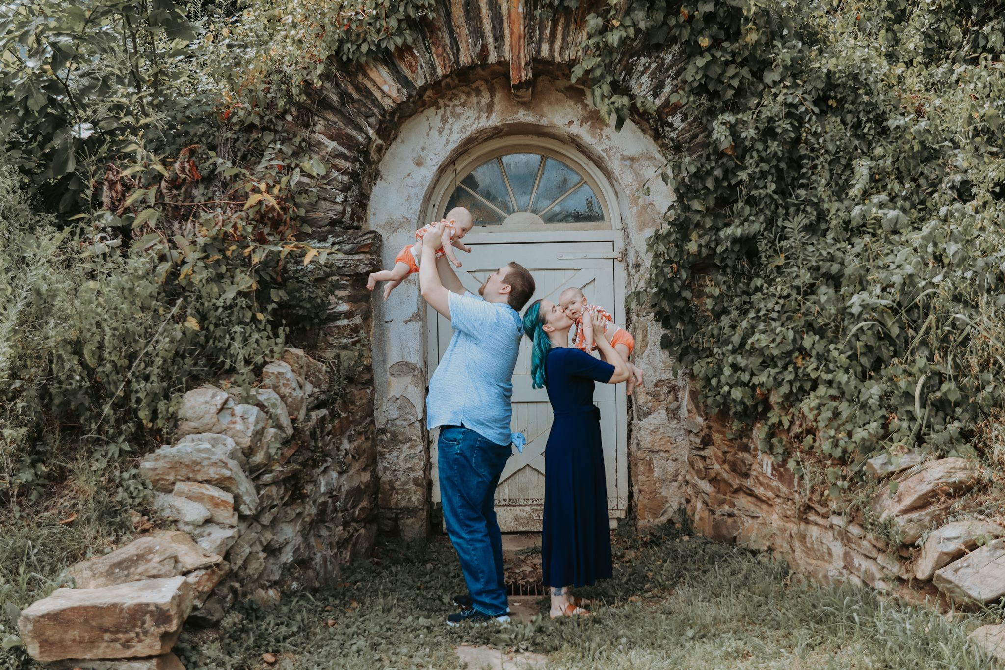 Playful couple posing under stone archway surrounded by greenery.