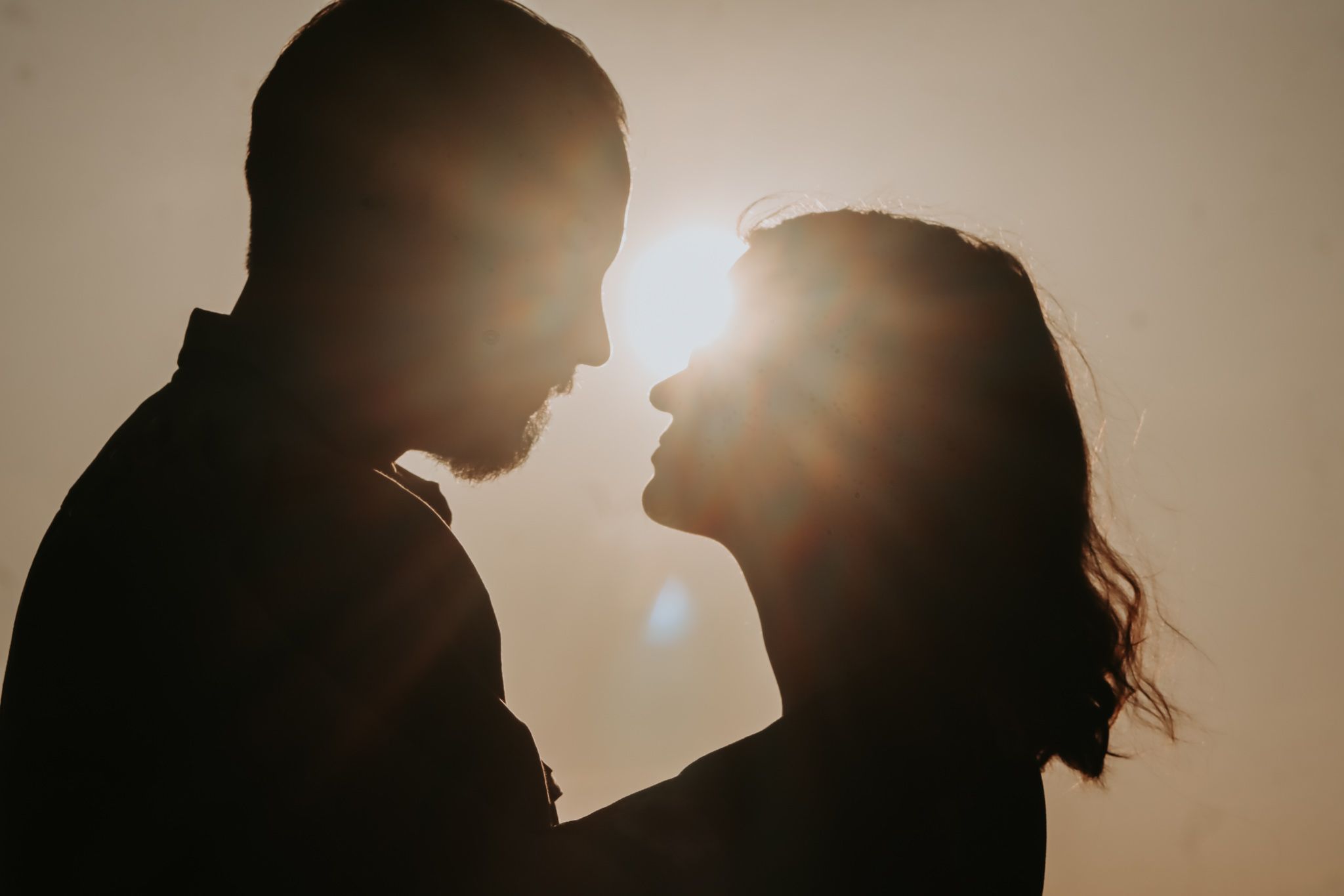 Silhouetted couple in romantic pose with sun flare between them.