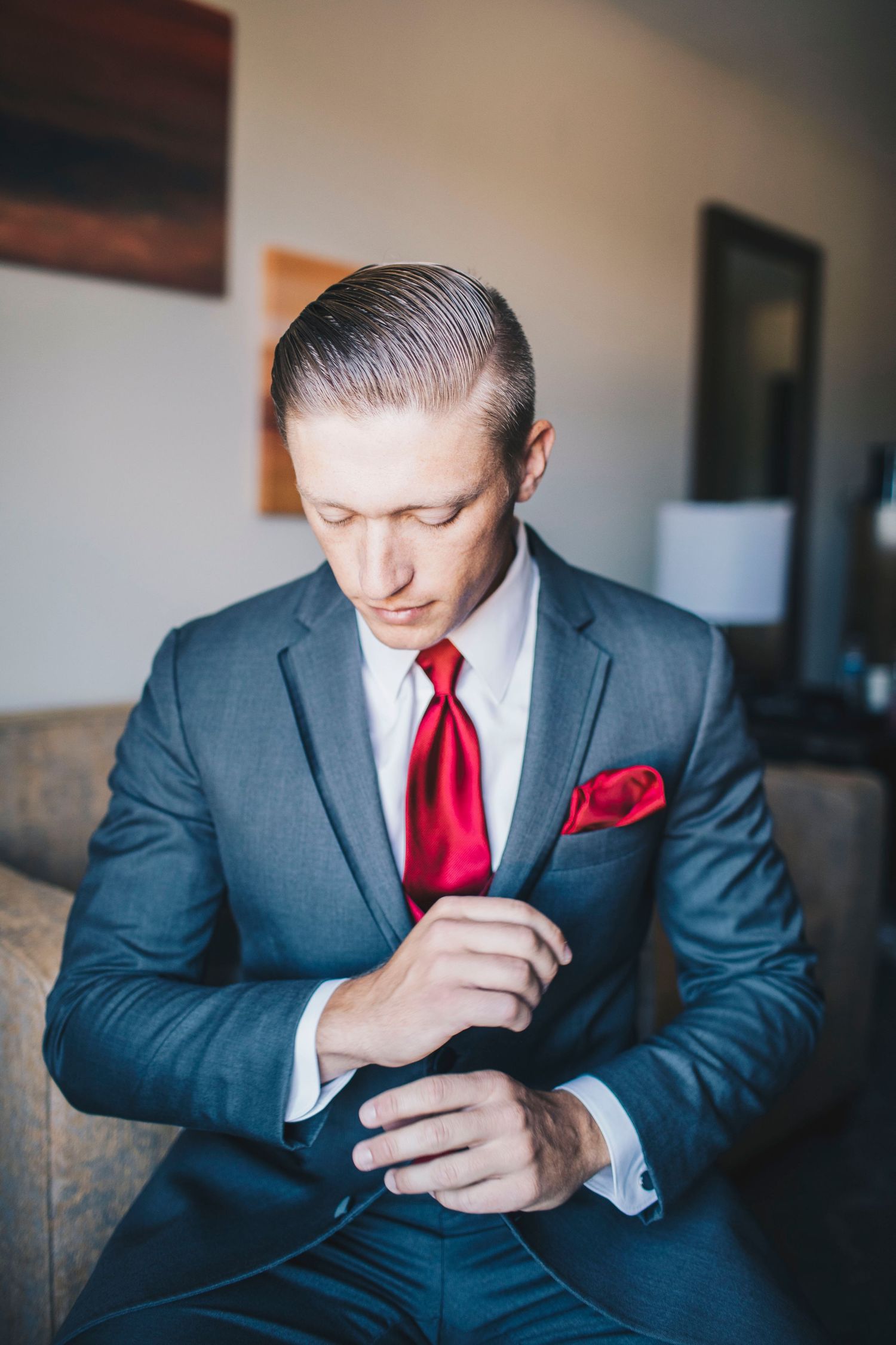 Groom in gray suit fastening cufflinks while seated before his wedding ceremony.