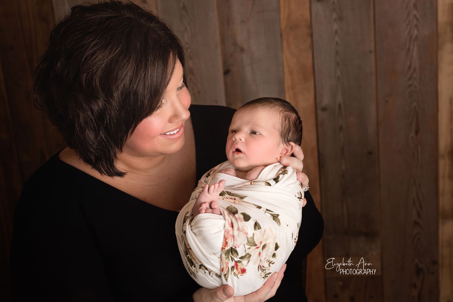 Beautiful mother looking at her newborn daughter, floral wrap and barnwood backdrop; Elizabeth Ann Photography Wisconsin