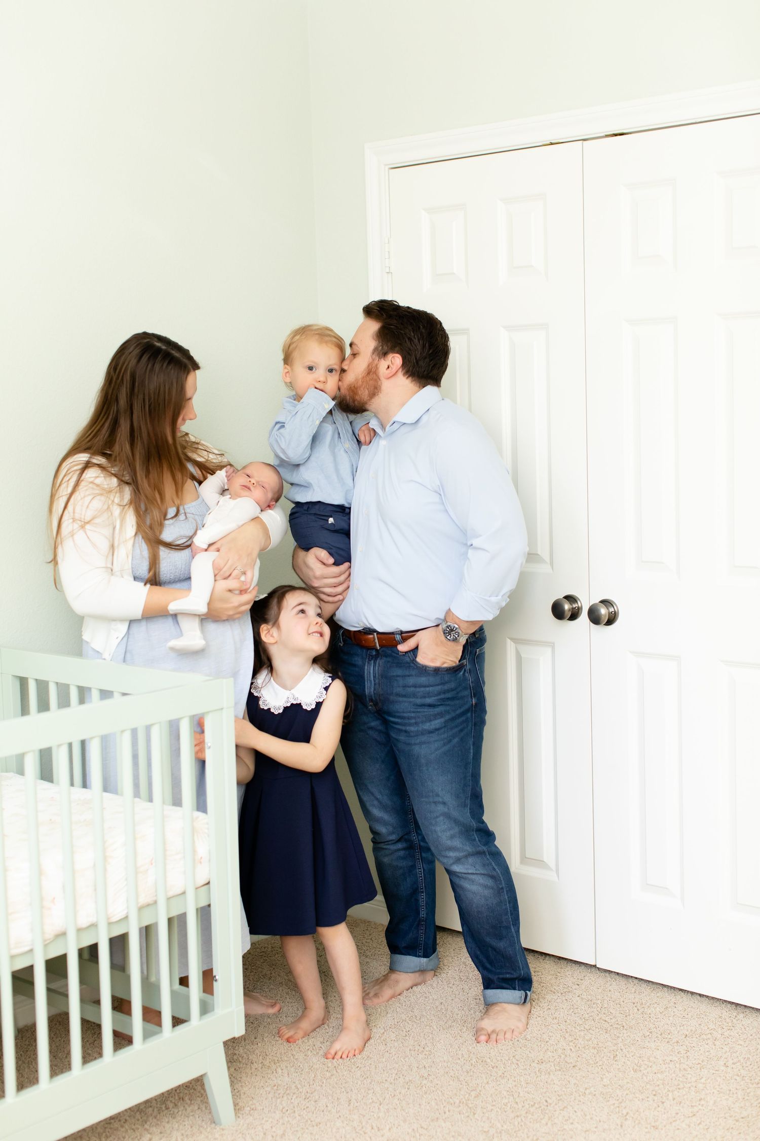 Casual family portrait in nursery room next to white crib.