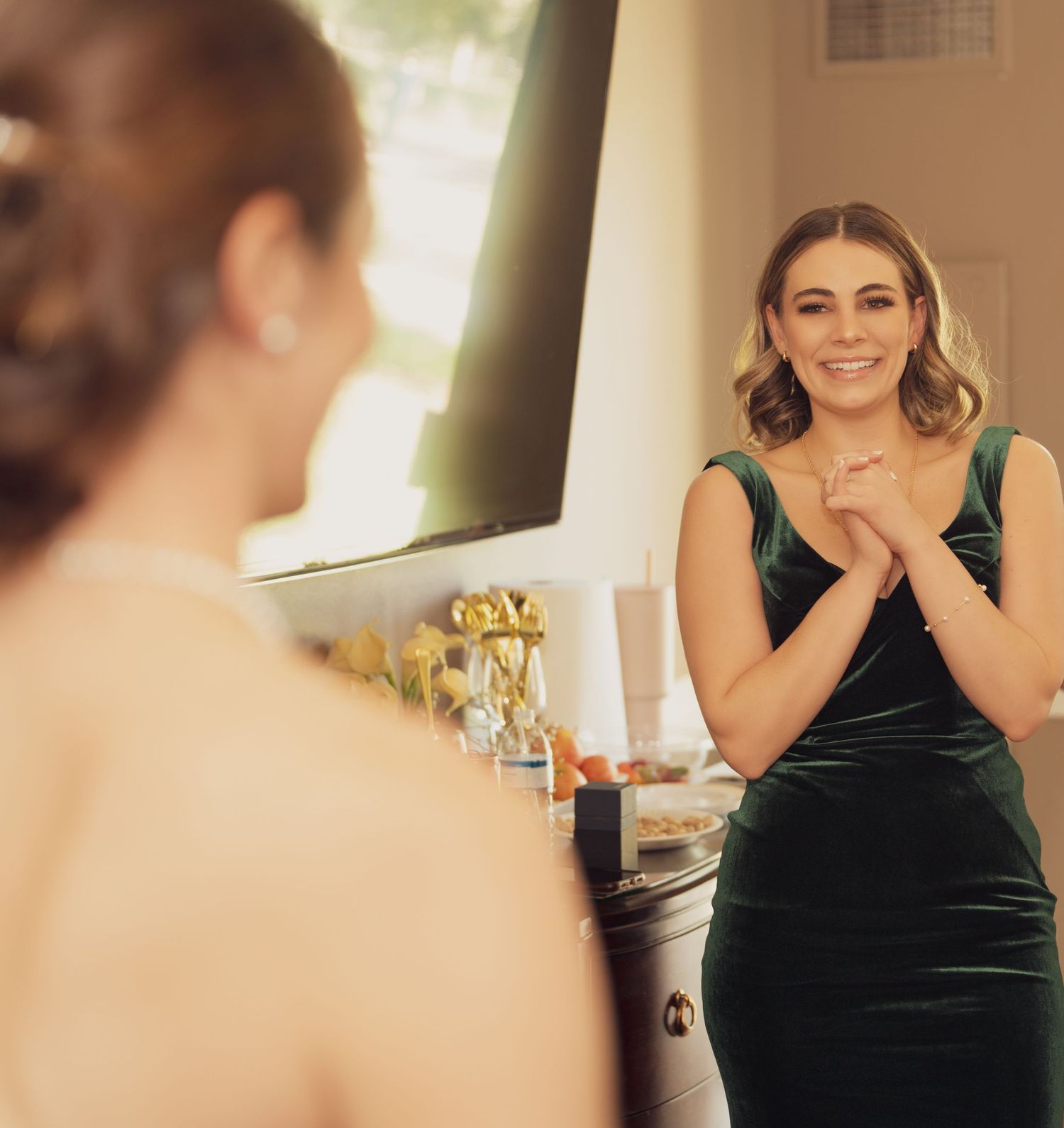 A person wearing an emerald green velvet dress stands joyfully in a softly lit indoor setting.