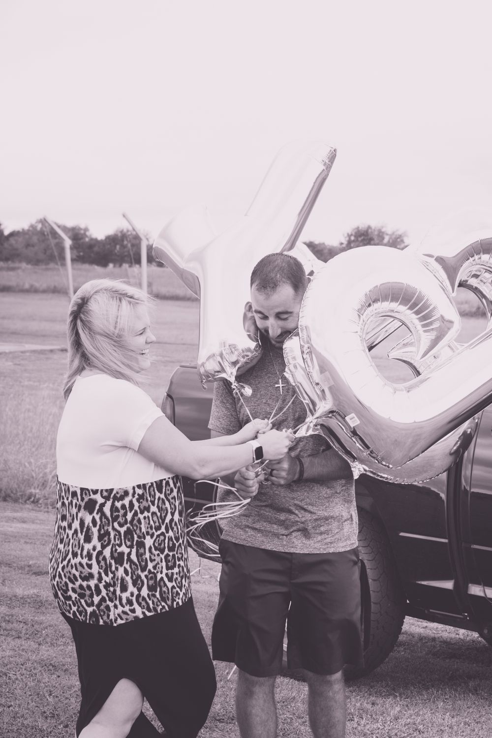 Two people celebrate with silver balloon letters in black and white photo.
