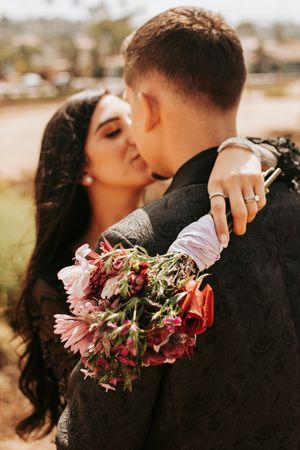 Romantic couple embracing with pink floral bouquet against natural backdrop.