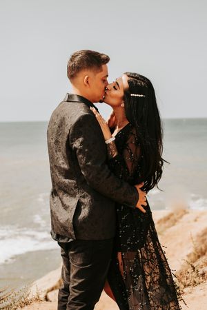 Couple in dark attire sharing romantic moments by coastal cliffs.