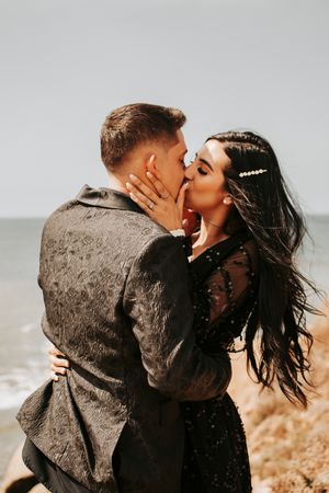 Couple sharing romantic moments against seaside backdrop with warm lighting.