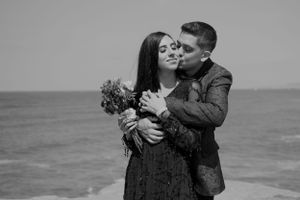 A romantic couple embraces on a beach in black and white as they share an intimate moment with a bouquet of flowers.