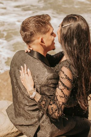 Romantic couple embracing in soft light against a sandy beach background wearing black lace and textured fabrics.